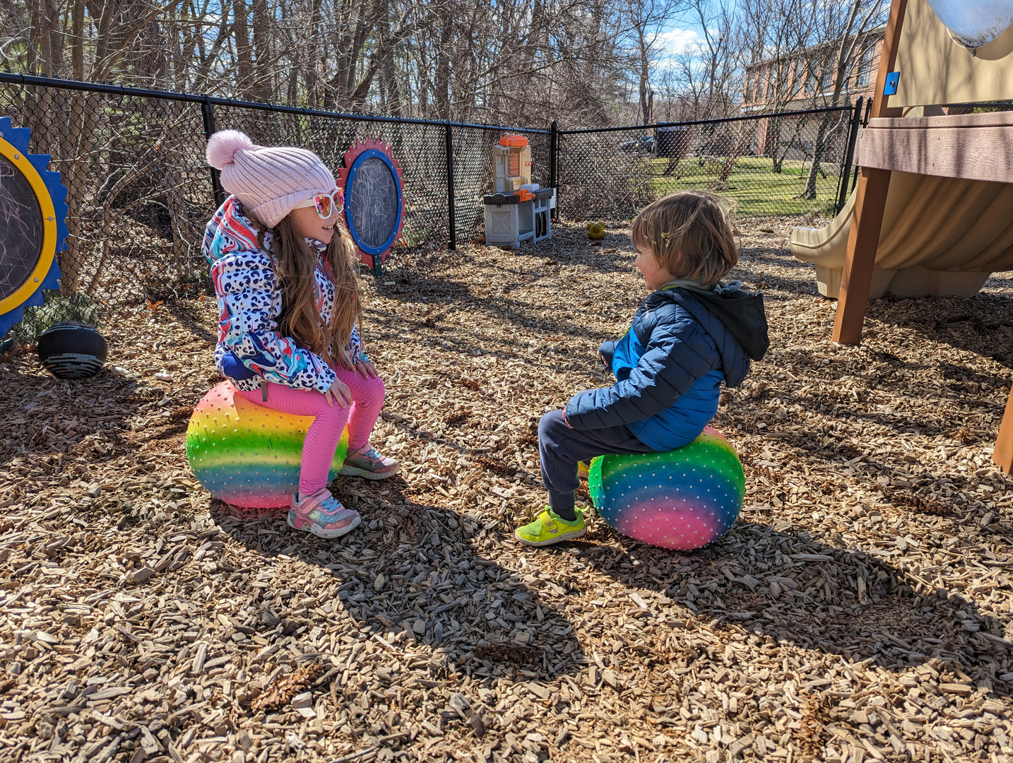 Two children chatting while sitting on colourful bouncing balls outdoors