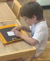 Child tracing letters in a sand tray