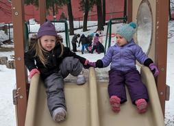 Two children happily going down the slide in winter